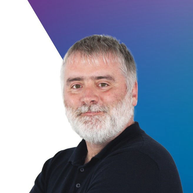 A white bearded very handsome man smiles against a white and blue backdrop